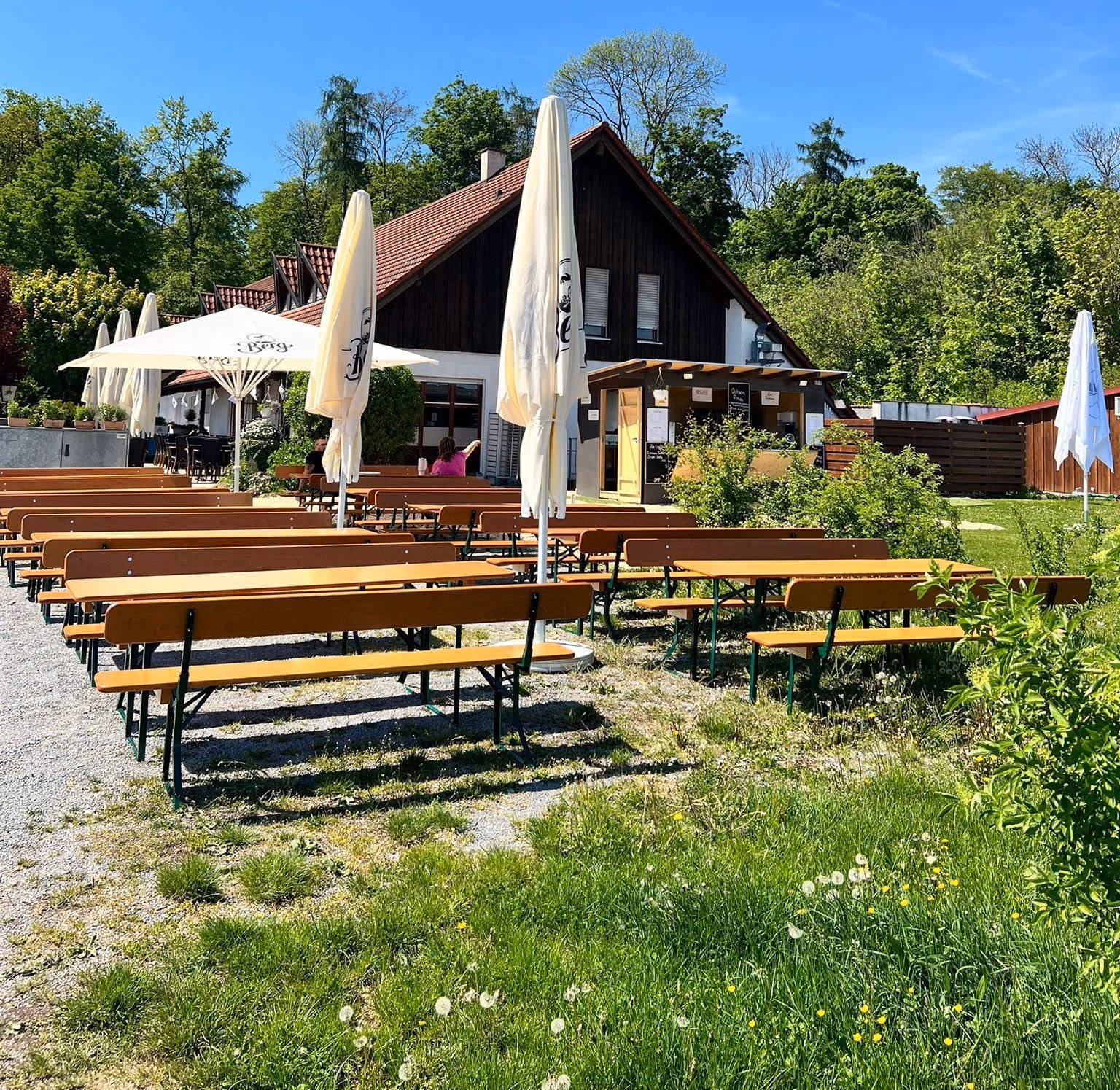 Biergarten mit Holzbänken und Sonnenschirmen vor dem Schützenhaus am Eichwald, dahinter der Wald
